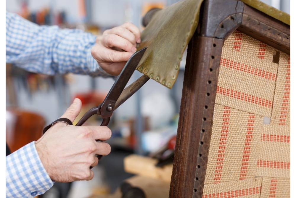 Person cutting fabric with shears on a chair being reupholstered